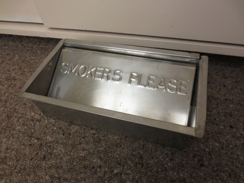 A metal floor ashtray with the inscription 'SMOKERS PLEASE'. A metal floor ashtray with the inscription 'SMOKERS PLEASE'.