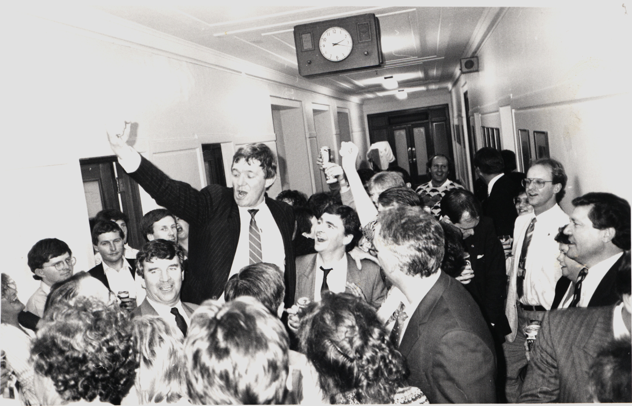 A black and white image of a corridor filled with people crowding around one person A black and white image of a corridor filled with people crowding around one person
