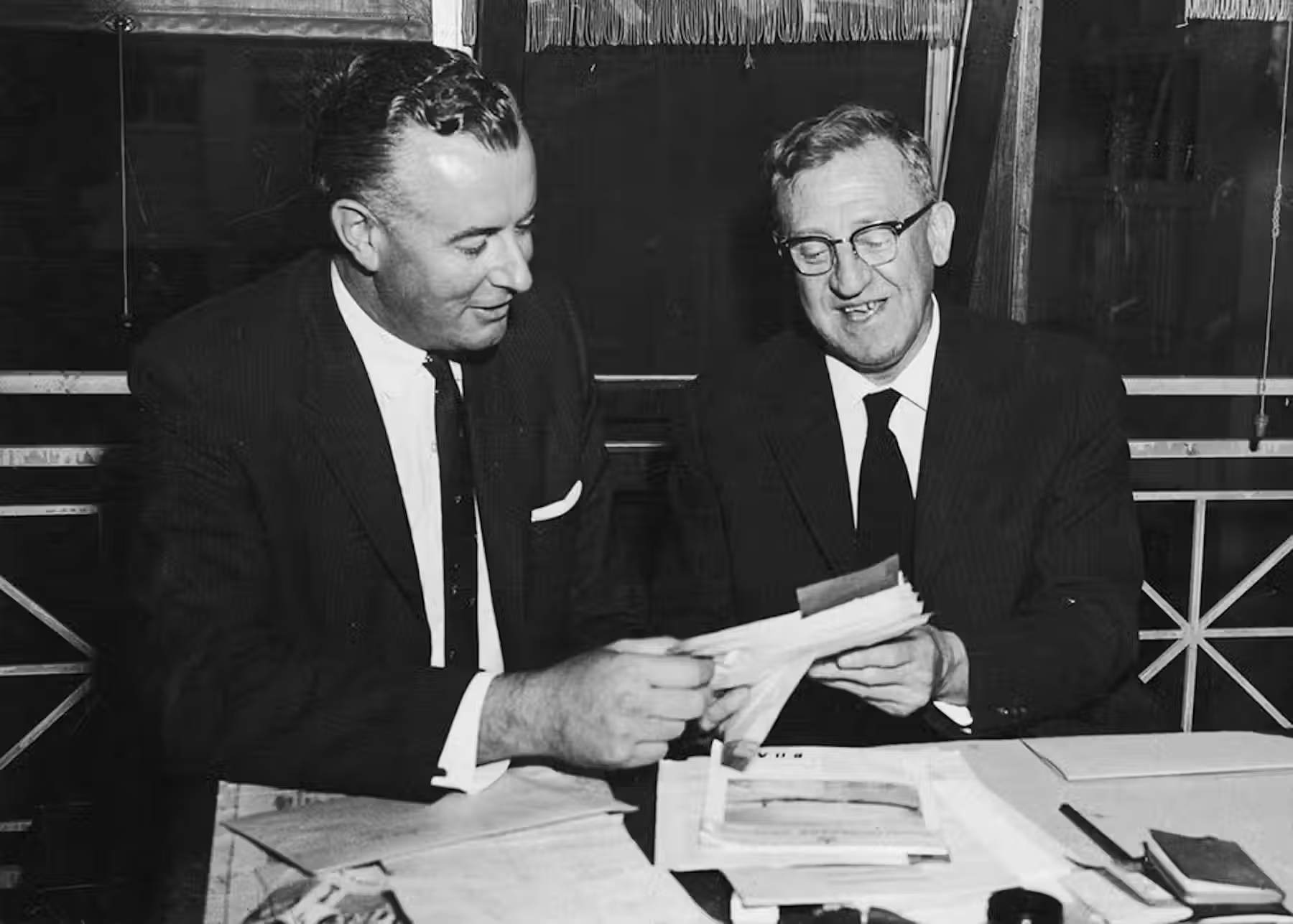 Gough Whitlam and Arthur Calwell sit next to each other, smiling, looking through paper documents together. Gough Whitlam and Arthur Calwell sit next to each other, smiling, looking through paper documents together.