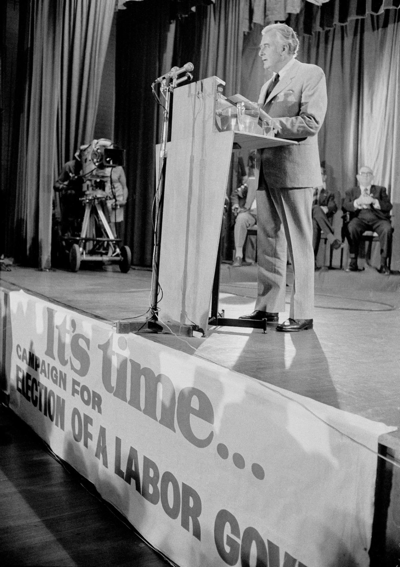 Gough Whitlam stands on a stage at a podium with a microphone launching Labor's election campaign. There is a large sign on the front of the stage which says, 'It's time... Campaign for election of a labor gov...' Gough Whitlam stands on a stage at a podium with a microphone launching Labor's election campaign. There is a large sign on the front of the stage which says, 'It's time... Campaign for election of a labor gov...'