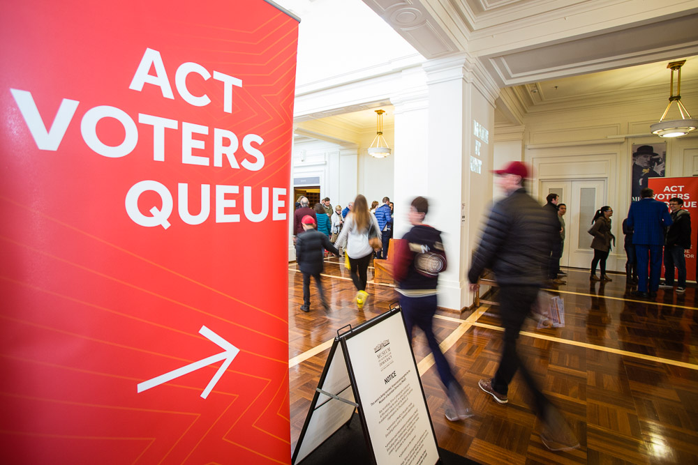 A red 'ACT voters queue' sign with an arrow directs people in King's Hall in Old Parliament House towards the voting area.