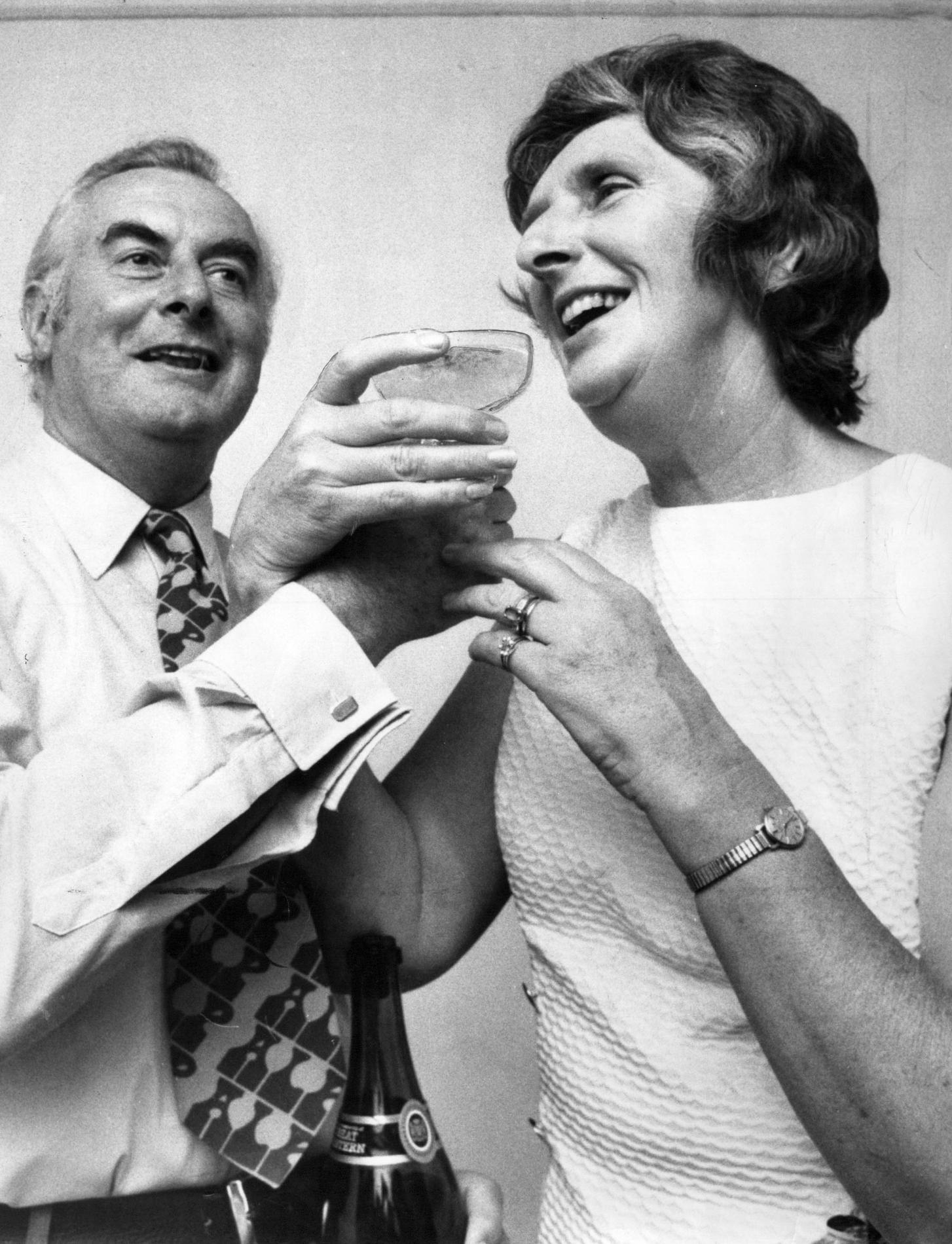 Gough Whitlam and Margaret Whitlam smile and hold a coupe of champagne between them. Gough Whitlam and Margaret Whitlam smile and hold a coupe of champagne between them.