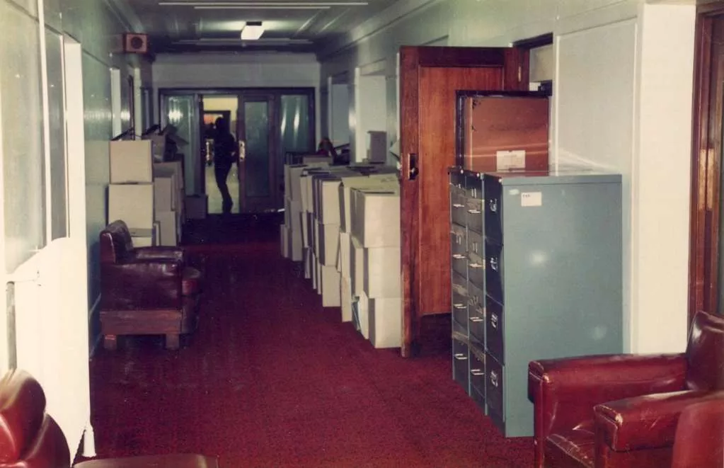 A red-carpeted corridor, lined with large cardboard boxes, filing cabinets and red leather furniture. A red-carpeted corridor, lined with large cardboard boxes, filing cabinets and red leather furniture.
